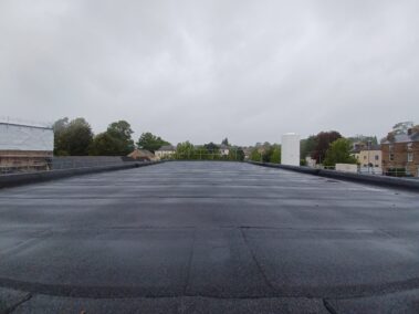 A wide-angle shot capturing the entirety of the refurbished roof, showcasing the seamless bituminous felt system and the sumped gutters.