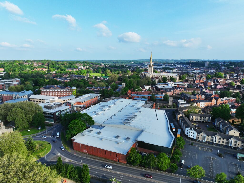 Aerial view of Norwich with a church spire, industrial buildings, and greenery.