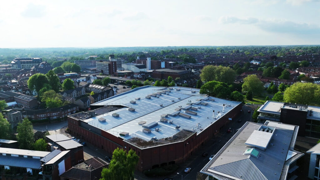 Aerial view of an industrial roof in Norwich, surrounded by trees and buildings.